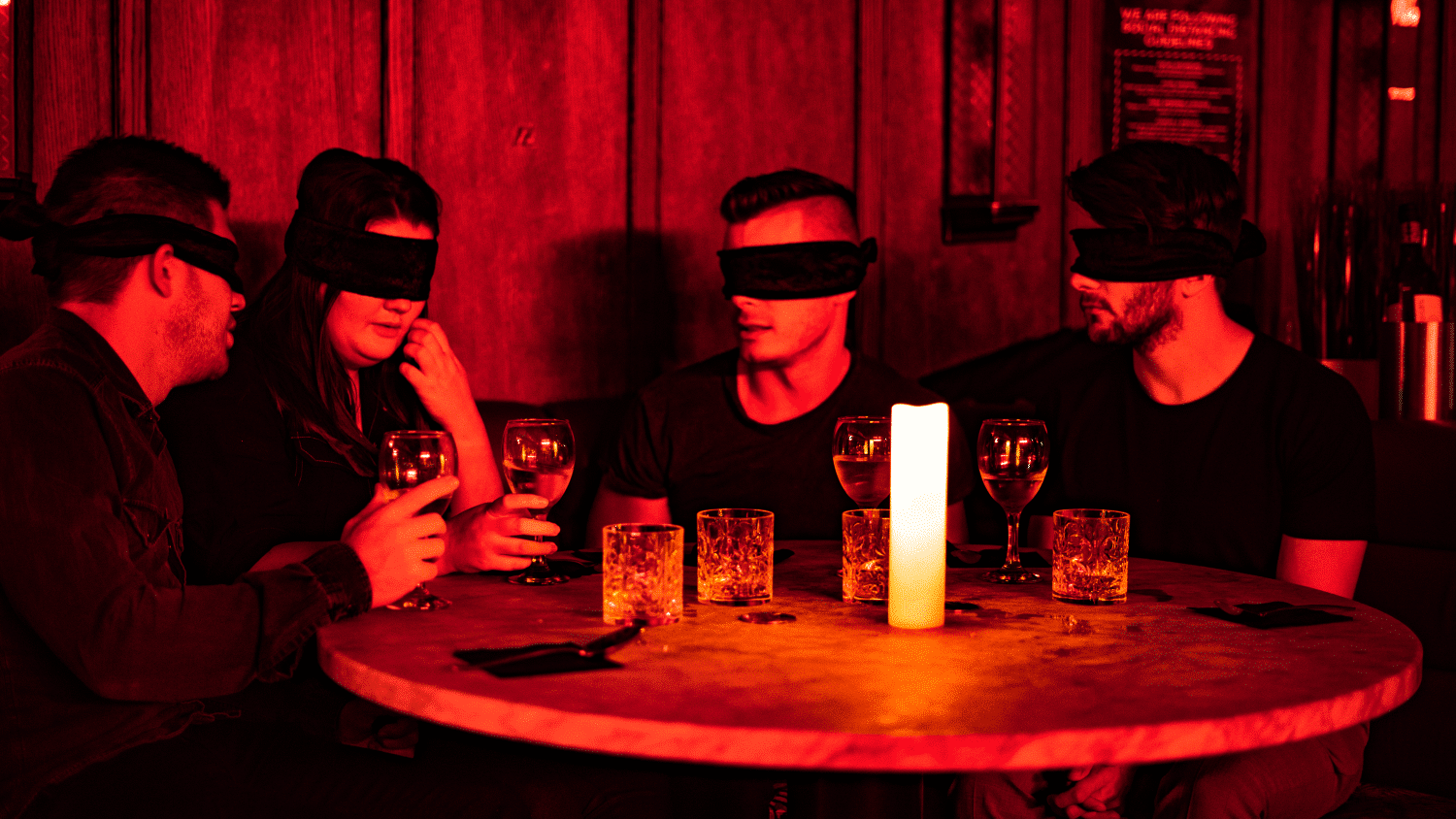 A group of four people sitting blindfolded at a table during the Dining in the Dark experience.