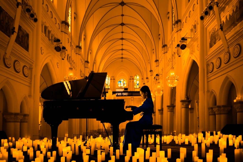 A photo taken from the center of the stage of a pianist playing the grand piano surrounded by countless candles with the high arches of CHIJMES in the background