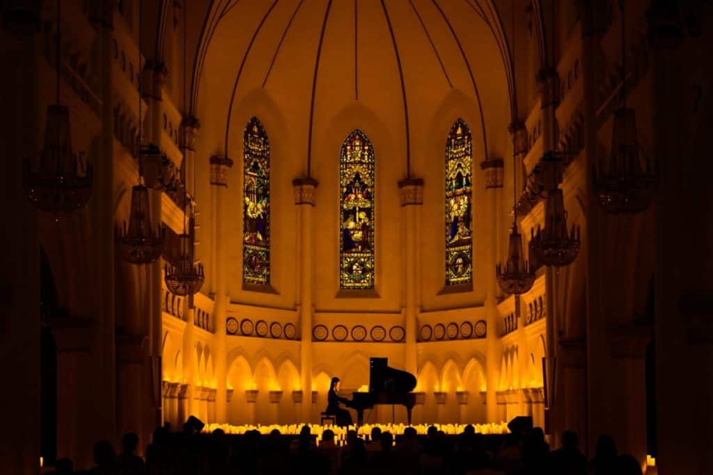 A wide shot of a makeshift stage at CHIJMES Hall's sanctuary taken from the audience featuring a pianist playing the grand piano while surrounded by hundreds of candles