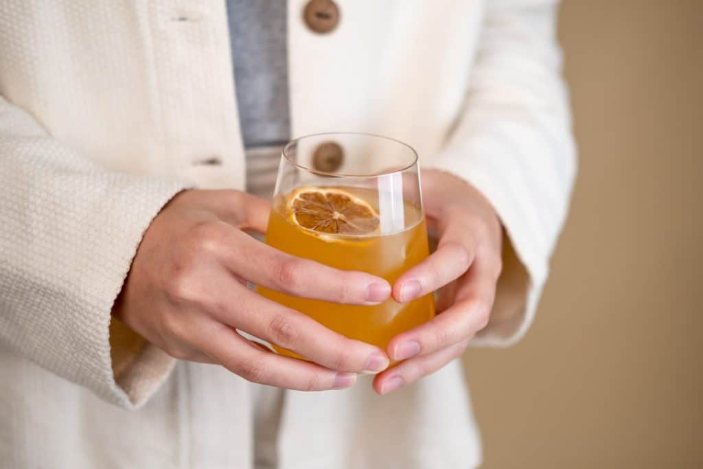 person holding a glass of orange kombucha