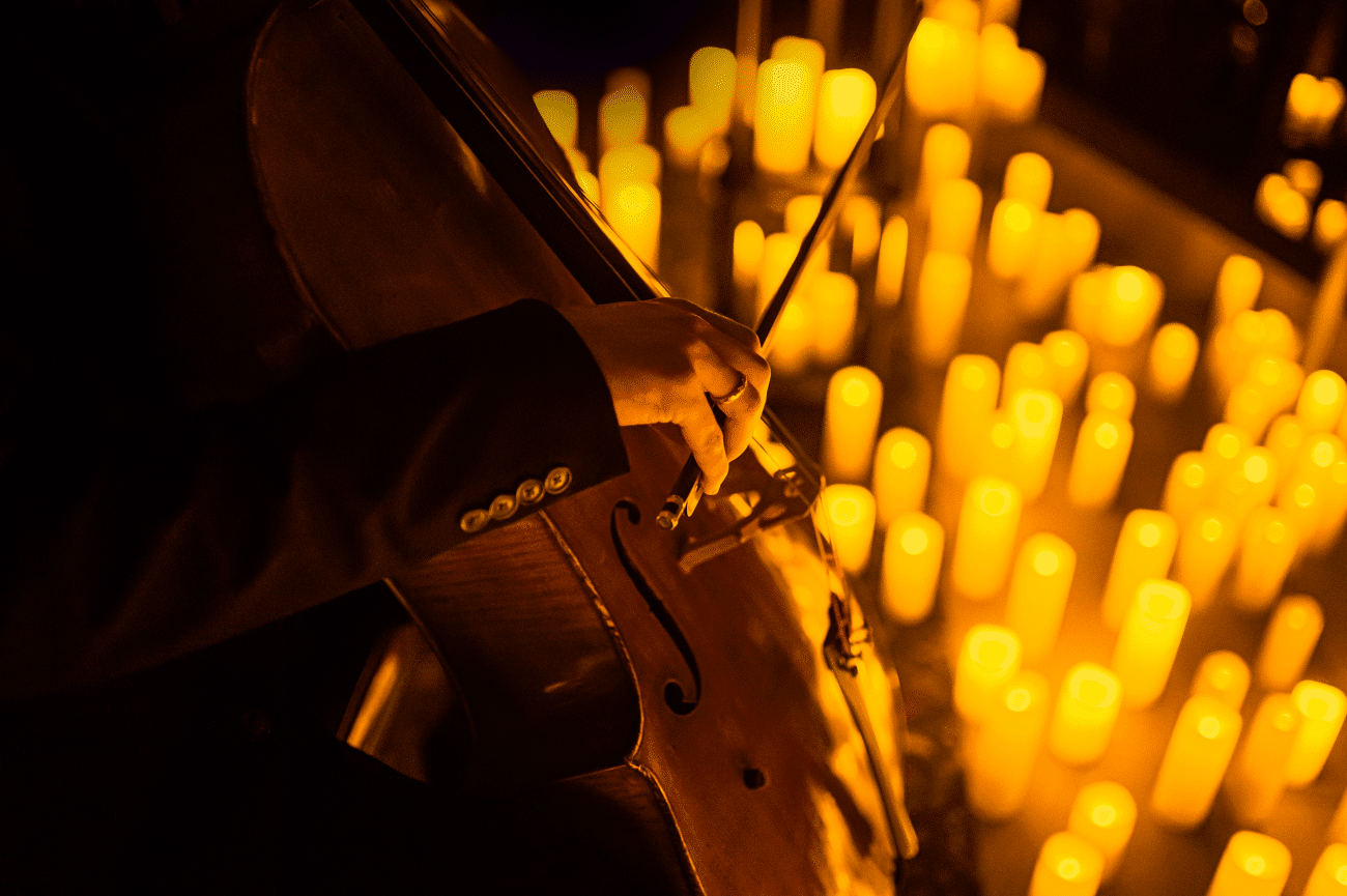 A close up of a man playing the cello with candles beside him.