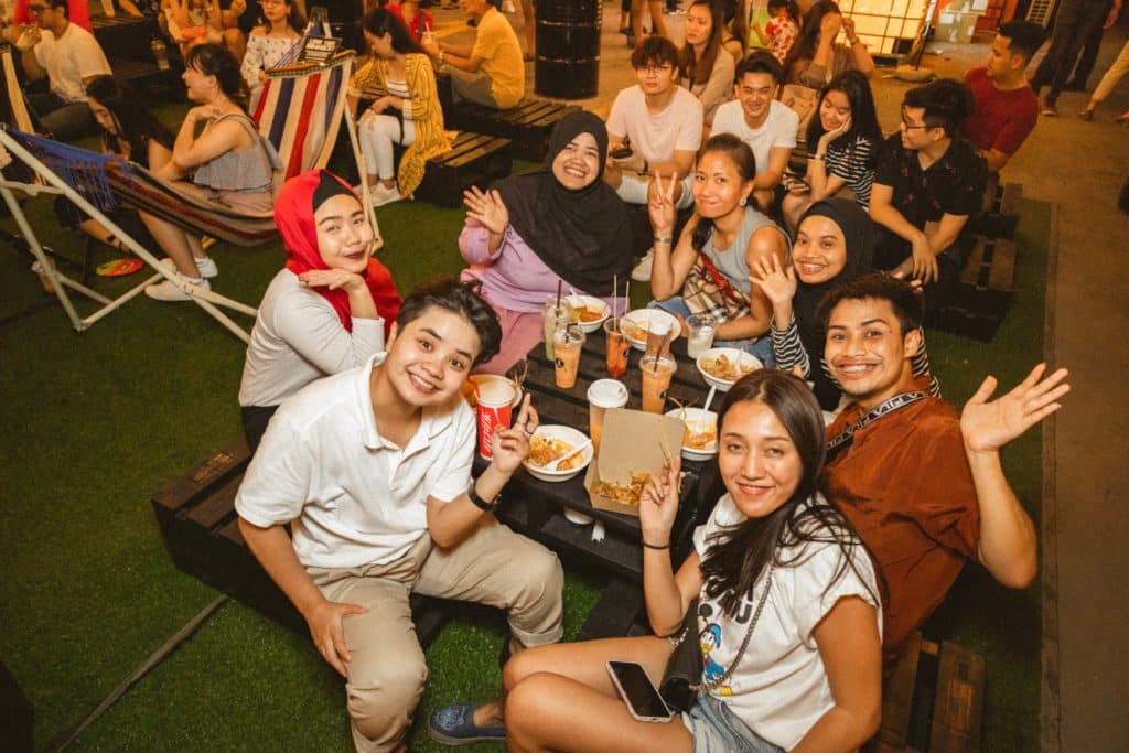 group of people sitting at artbox singapore, posing for photo, around a low table loaded with heaps of street food