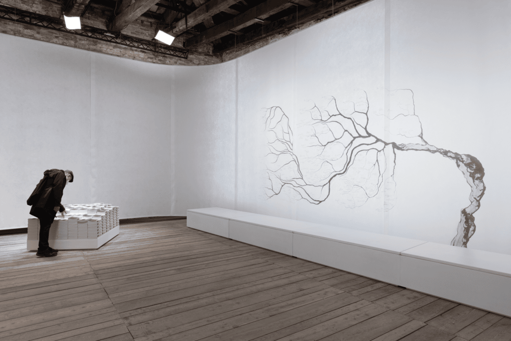 person bent over looking at artwork in white room with leafless tree painted on wall