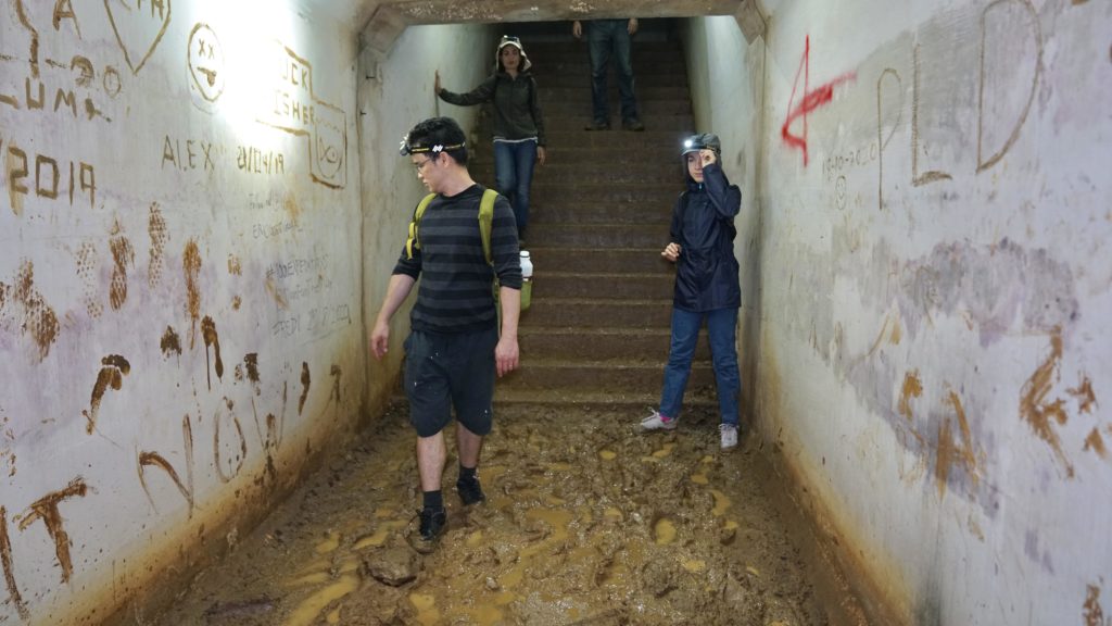 underground tunnel at Marsiling bunkers in singapore with a few people inside, ankle-high mud, graffiti on walls, with beyond expeditions