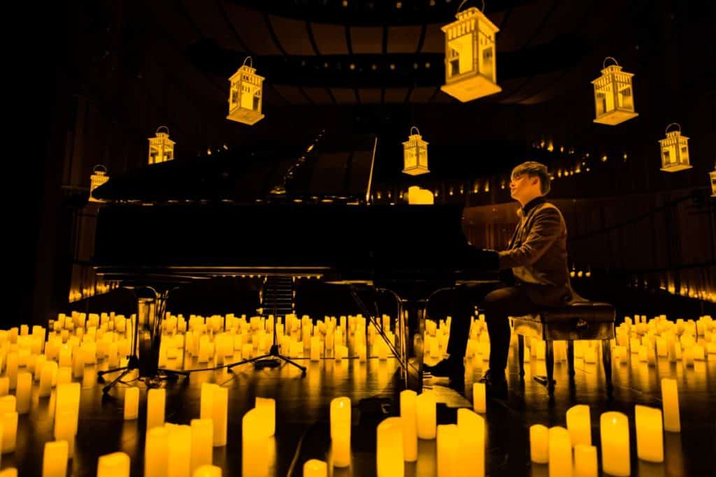 An upward shot of a pianist performing on stage surrounded by hundreds of candles with hovering lanterns above